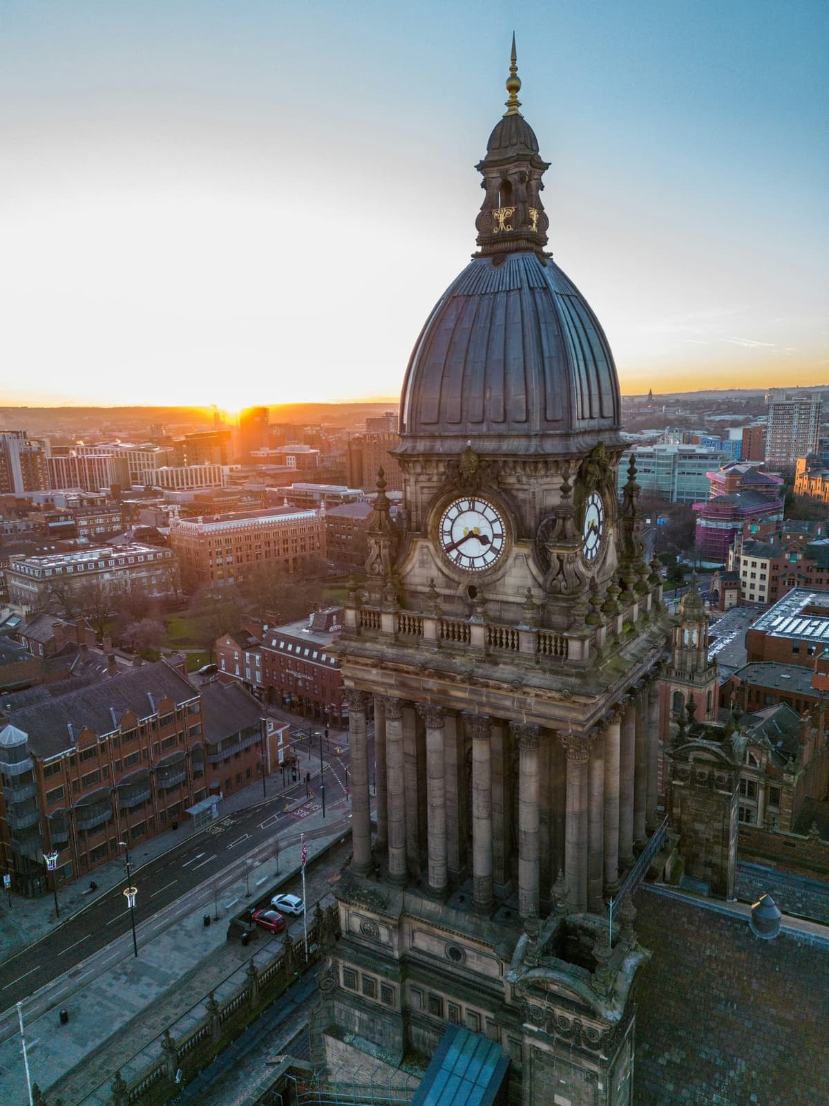 Leeds Town Hall's clock tower and dome at sunset, with the city streets below