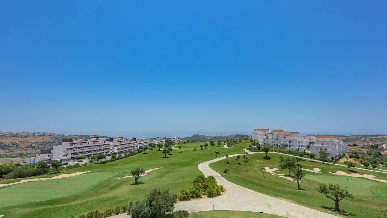 Golf course running down to white apartment buildings, with the sea on the horizon