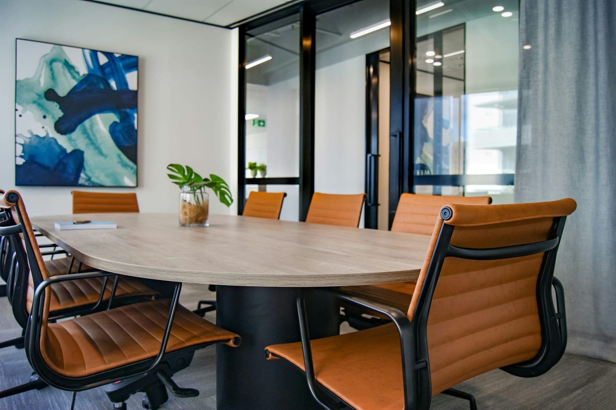 A quiet meeting room with an oval wooden table and tan leather chairs